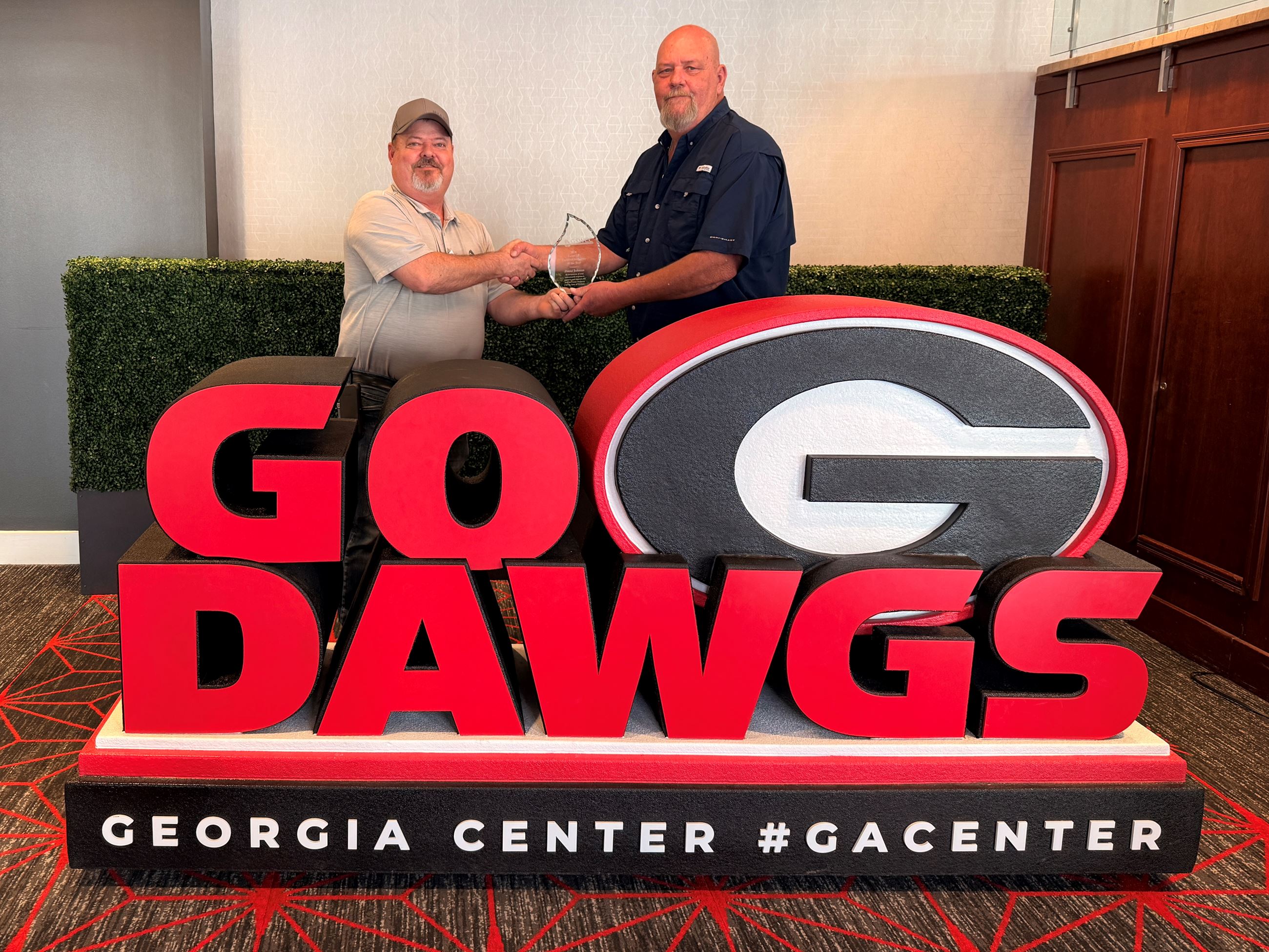 David and Chuck holding an award standing behind a sign that says Go Dawgs with the UGA logo