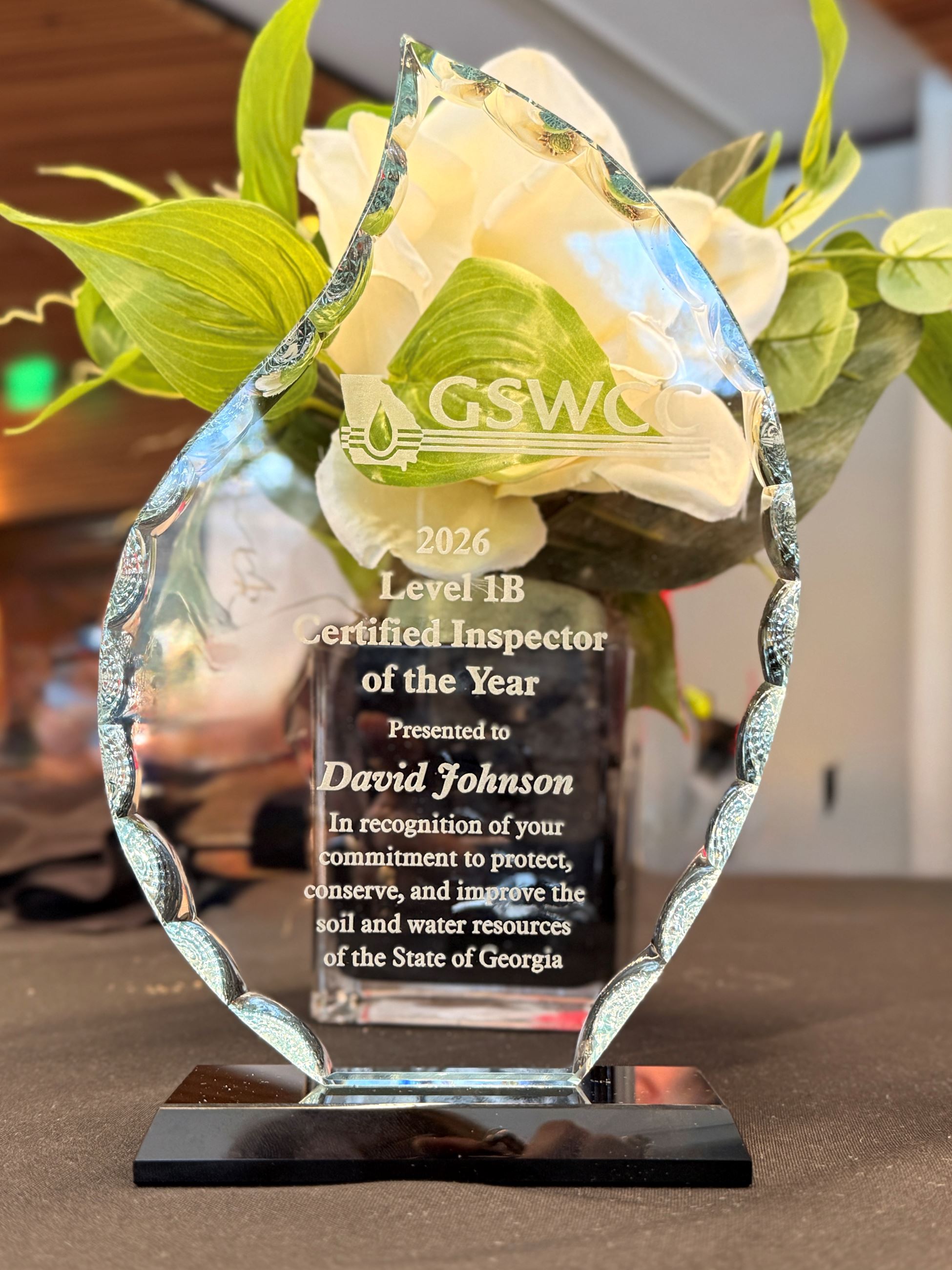 Acrylic award sitting in front of a white flower with green leaves